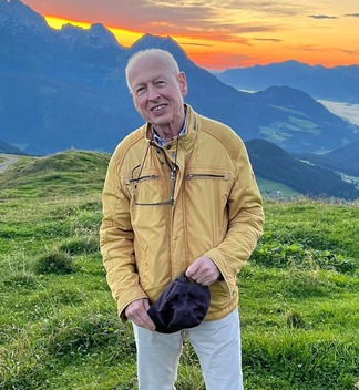 Dr. Franz auf einem Berg in Salzburg vor gelb-orangenem Sonnenuntergang.